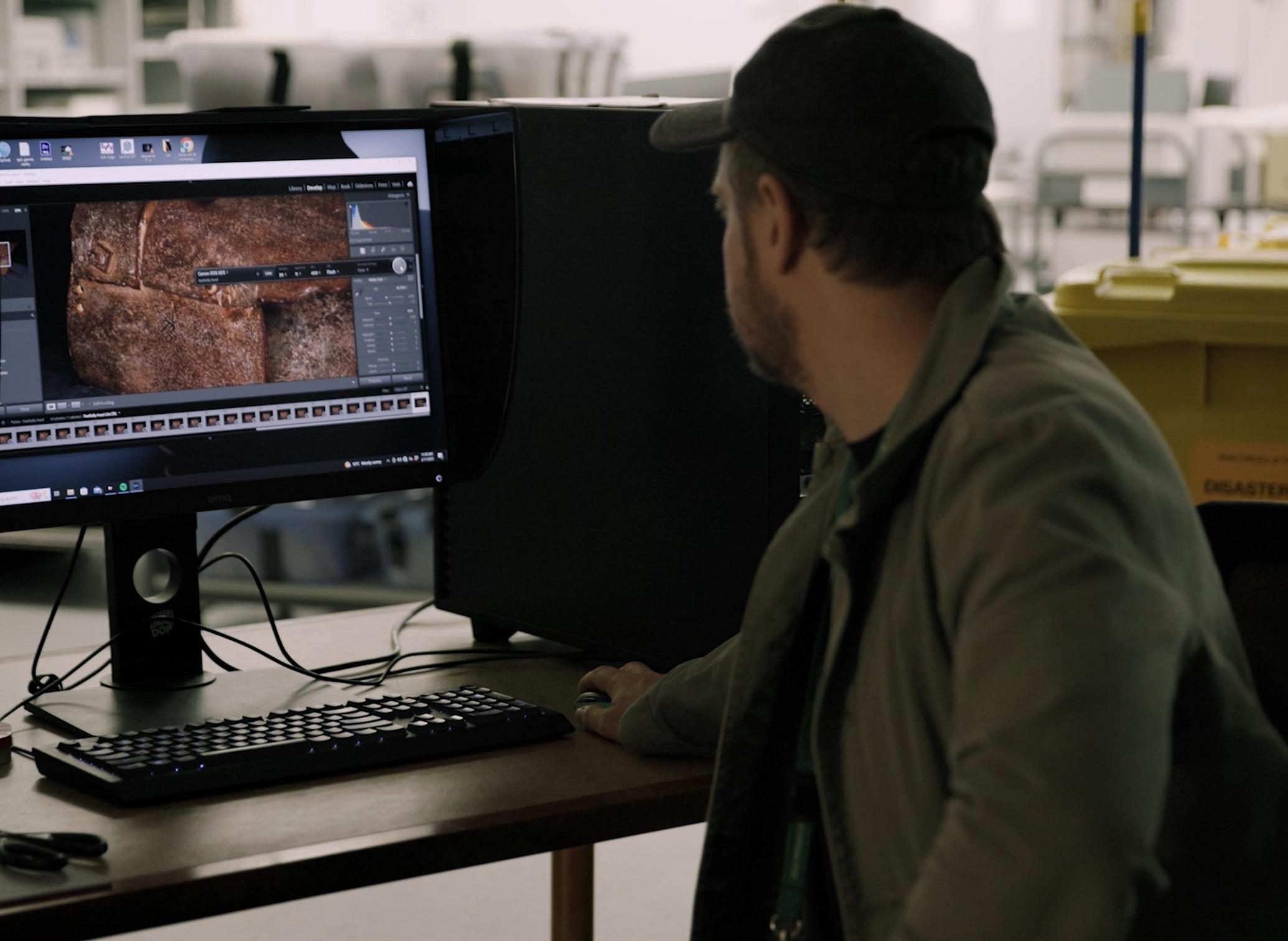 Man sitting at a desk looking at a computer screen showing Ned Kelly's armour.