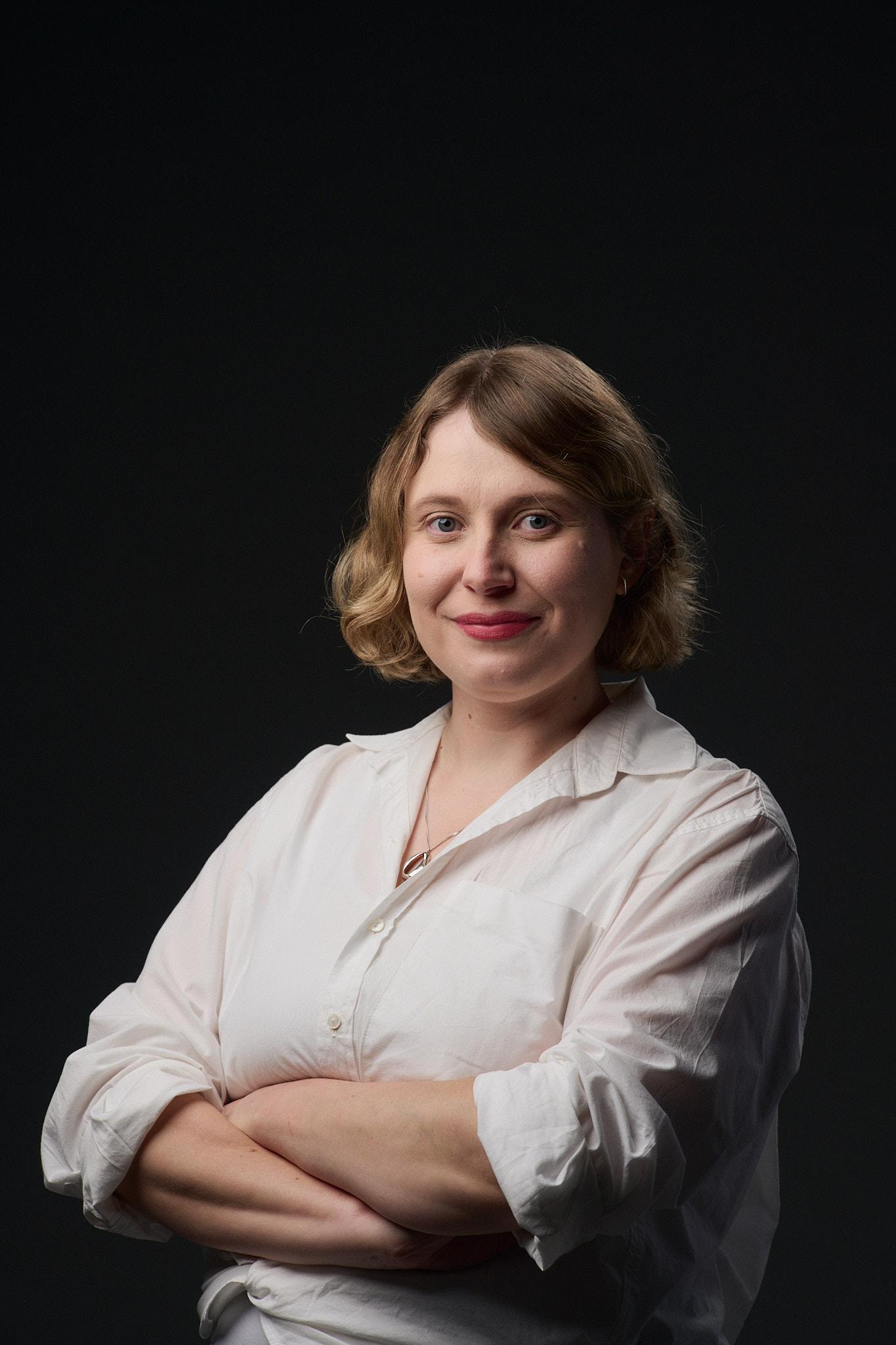 Headshot of a woman with short blonde hair, wearing a white shirt against a black background.