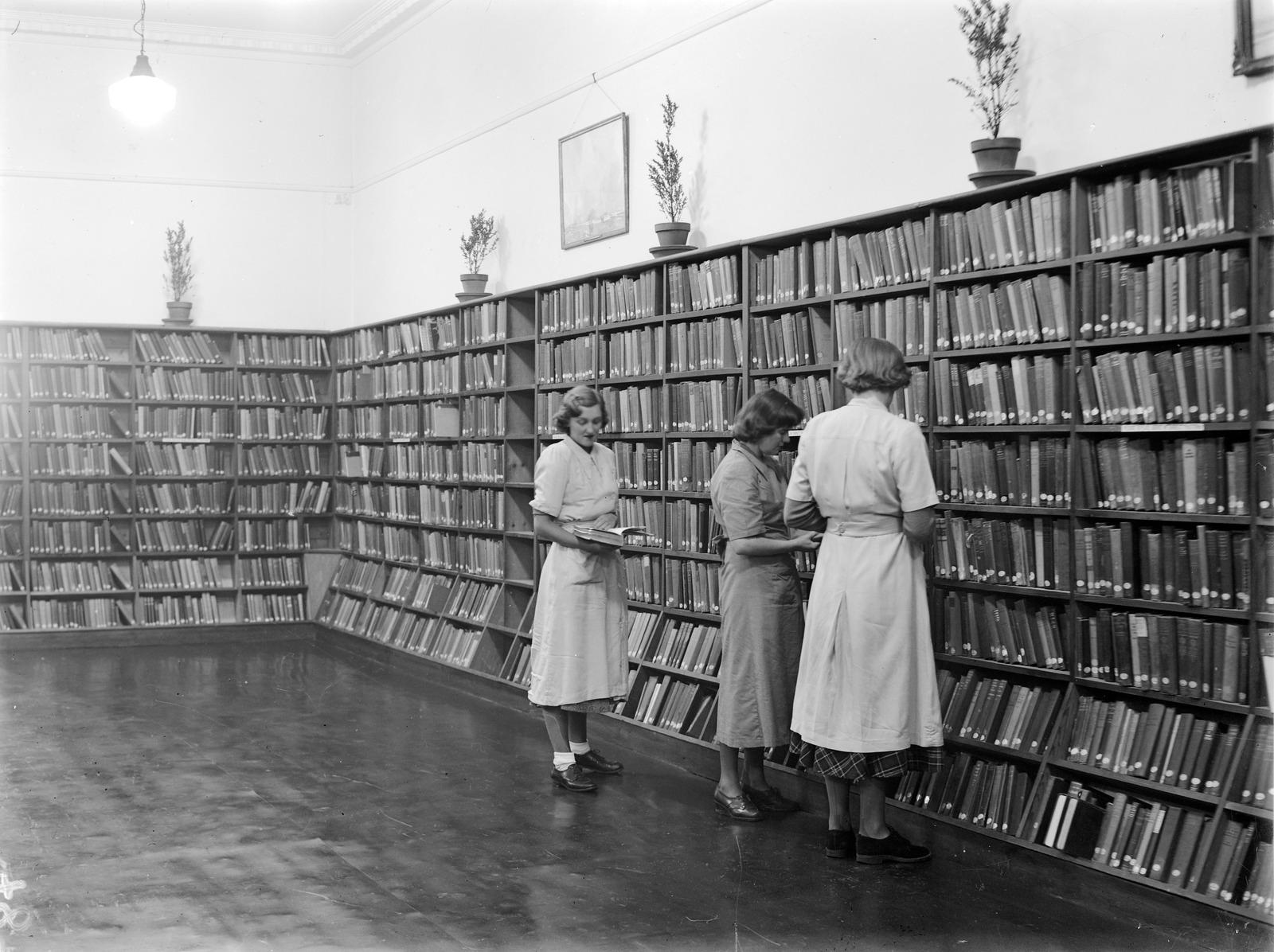 Archival image of people browsing books on a shelf in a library.