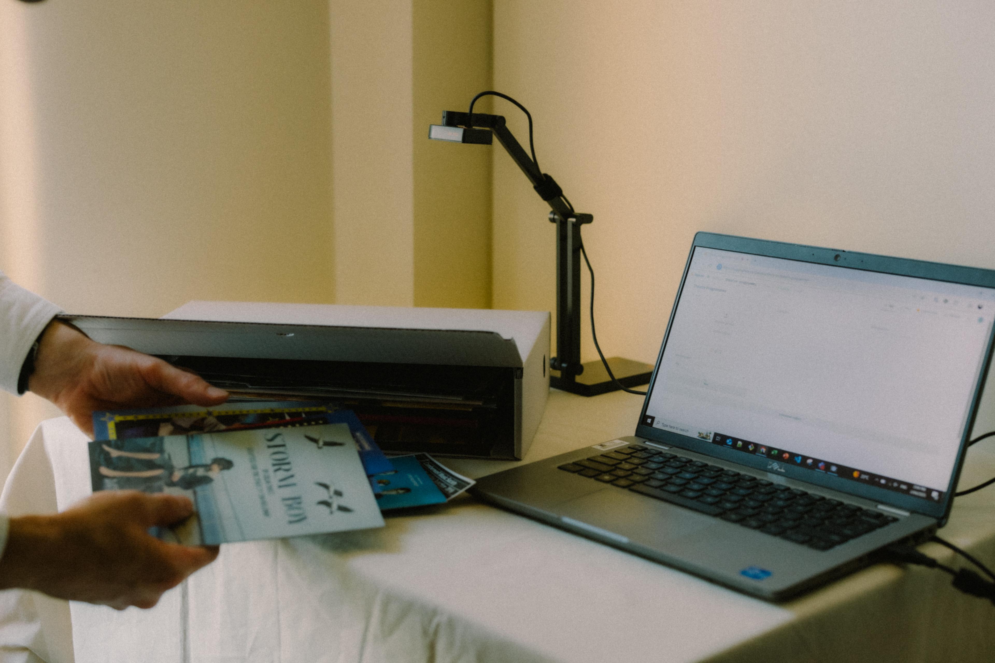 Two hands holding a document entitled "Storm Boy" in front of a desk with a laptop, small camera and an archival box.