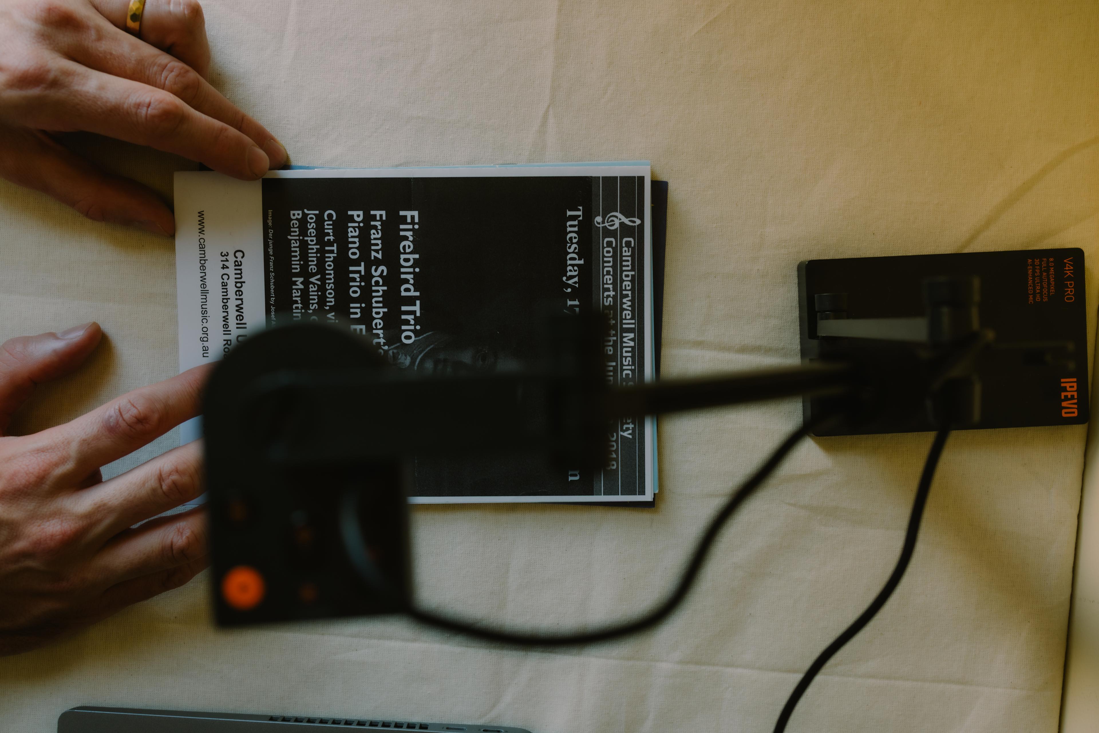 Top down view of an overhead small USB camera, with a theatre programme being lined up beneath it.