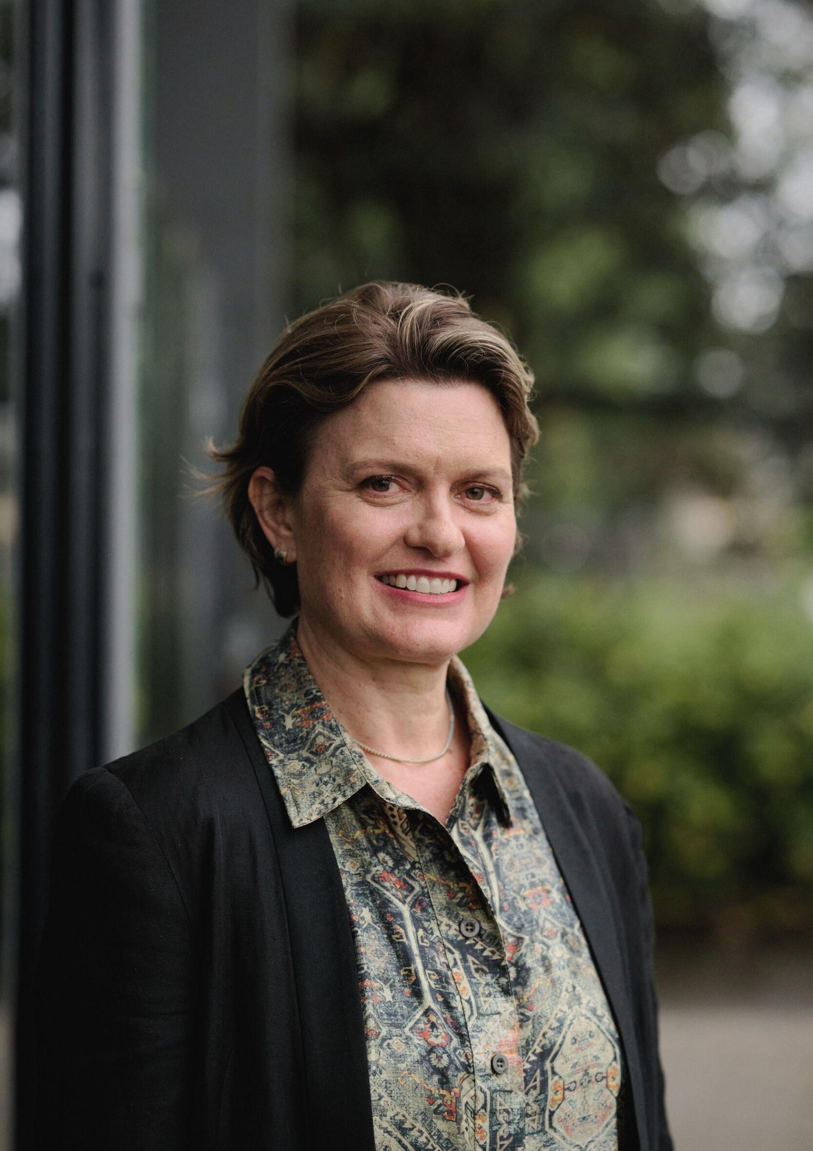 Headshot of a smiling woman in a patterned shirt and blazer, with chin-length brown hair.