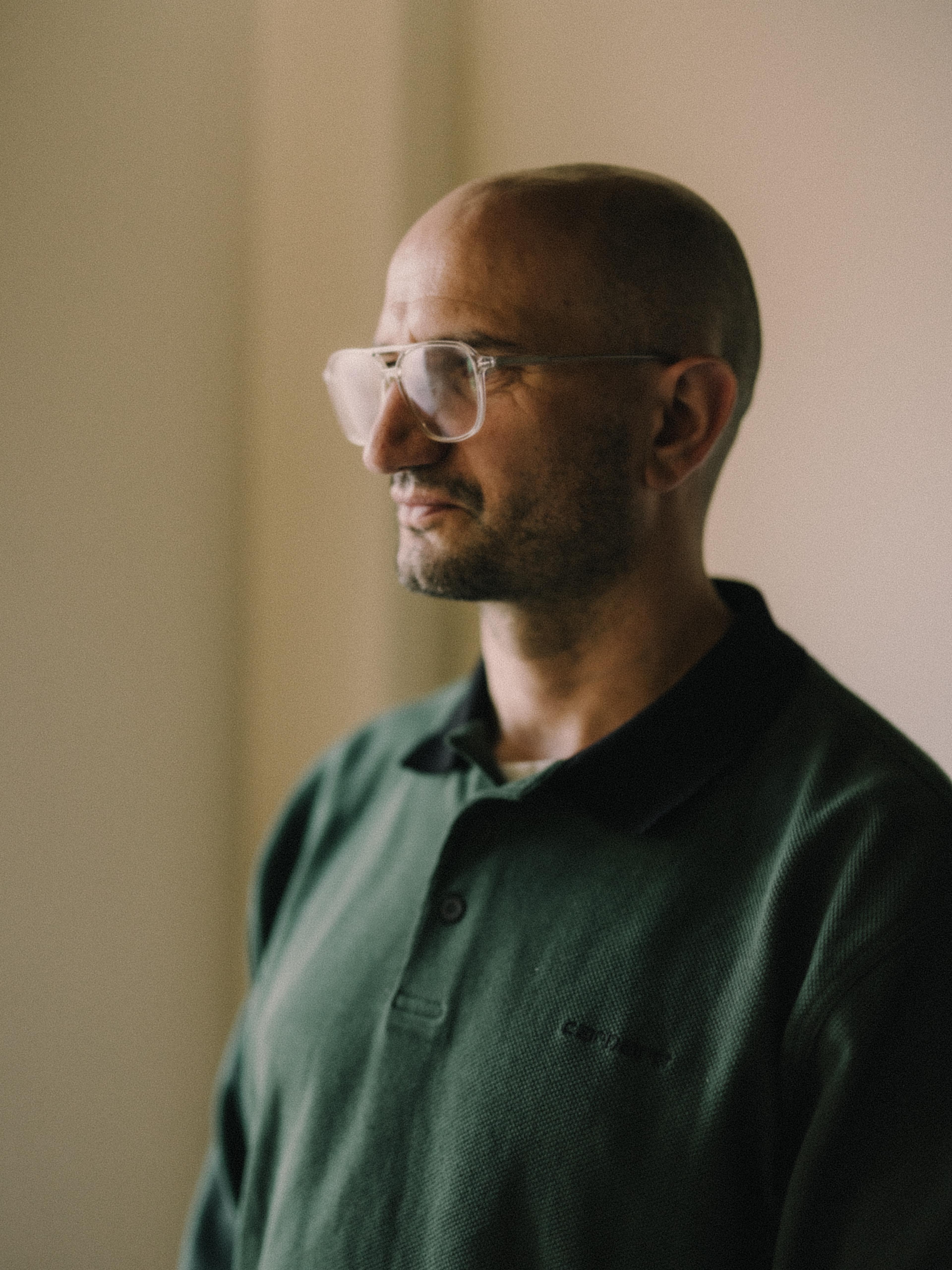 Headshot of a bespectacled man in a dark green, collared shirt, angled slightly away from the camera.