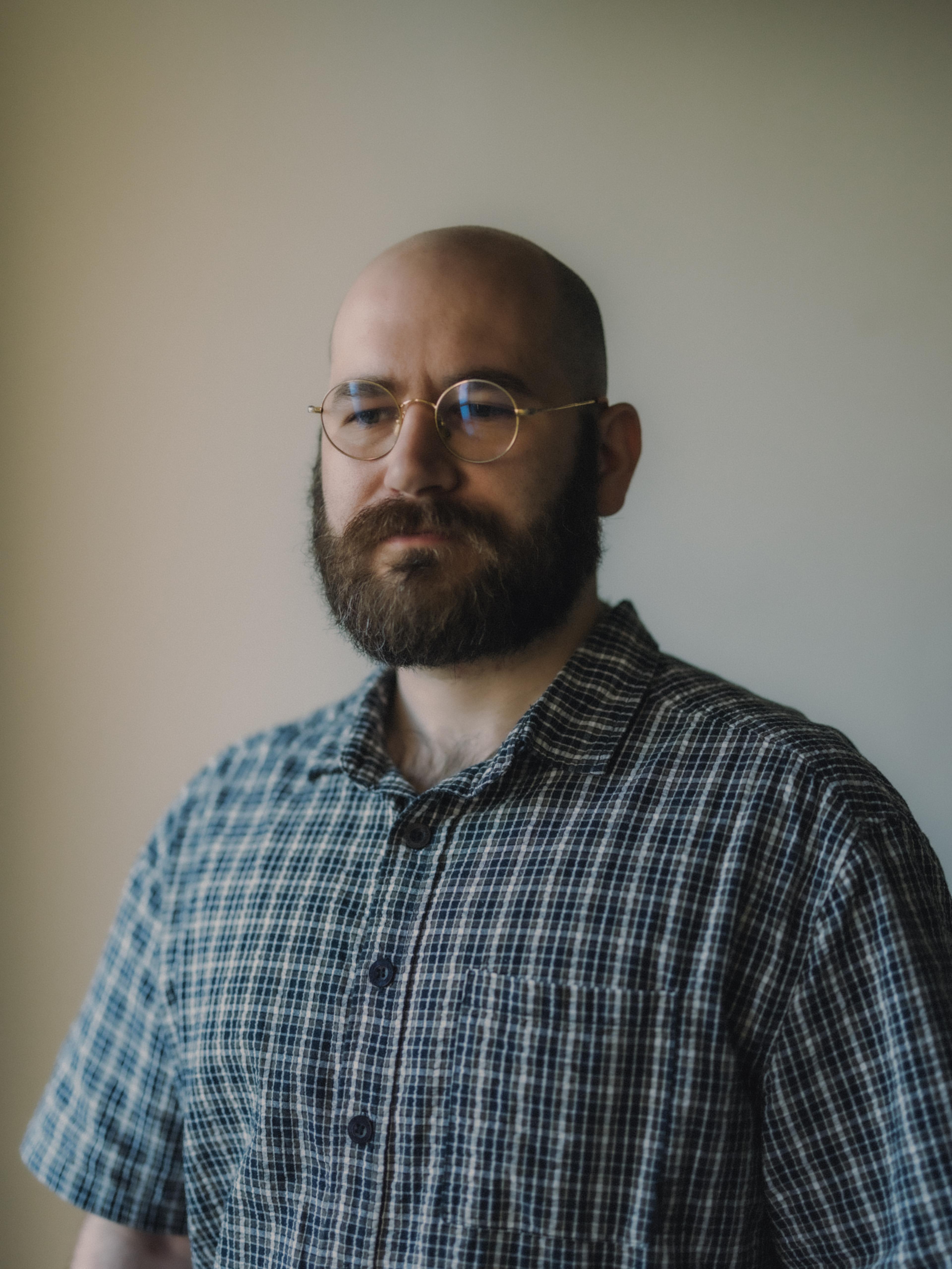 Headshot of a spectacled man with a thick beard, wearing a checked collared shirt.