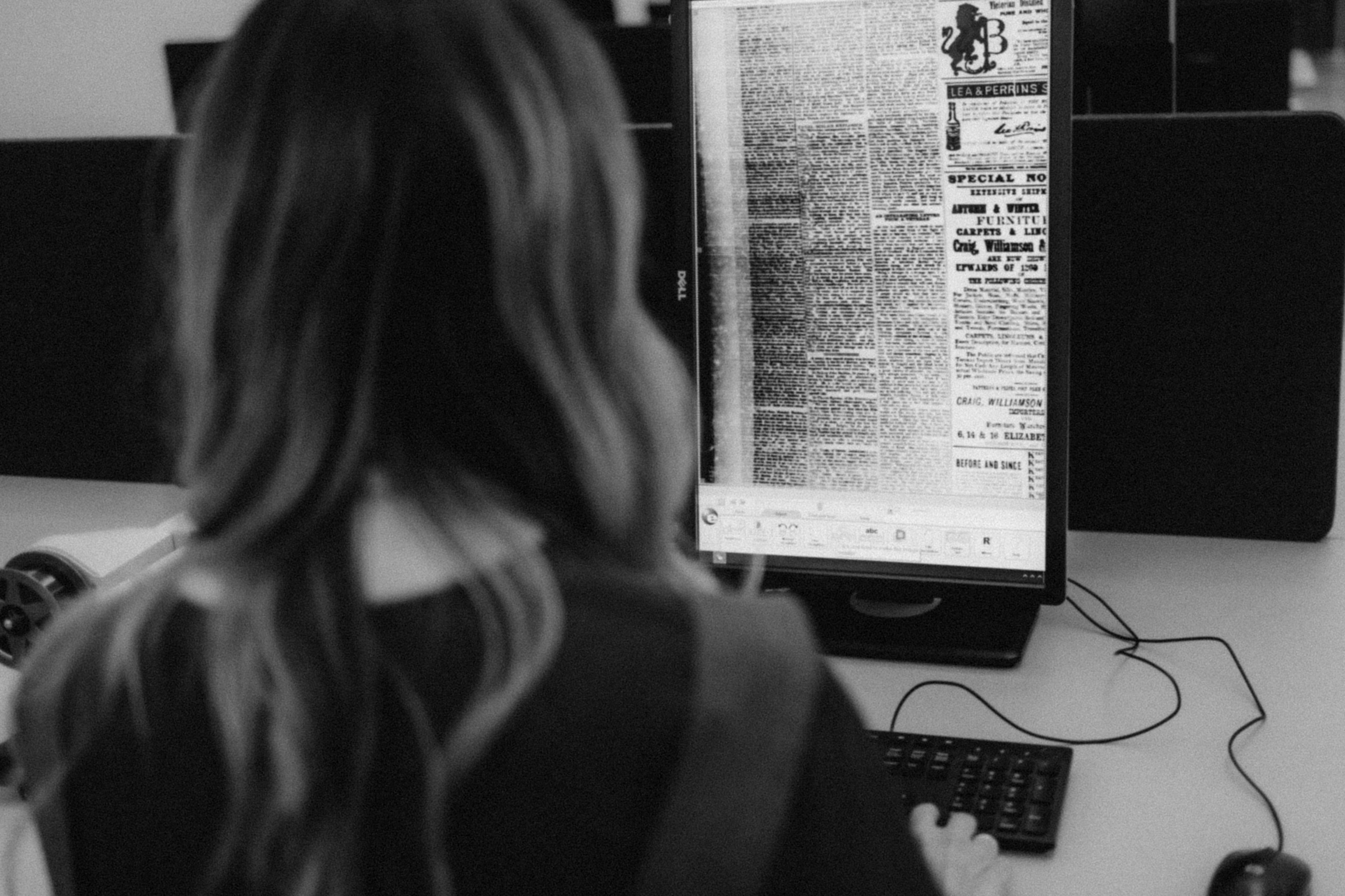 The back of woman's head as she observes blurred text on a computer screen.