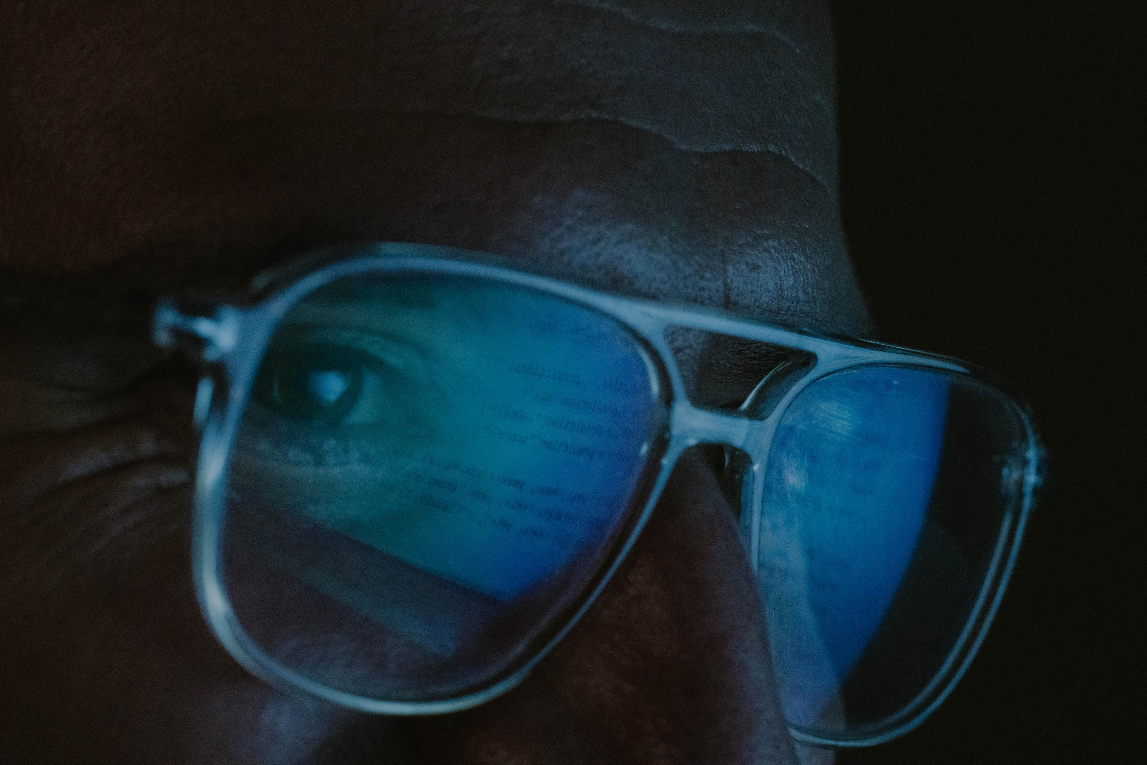 Close-up of a set of bespectacled eyes. The glasses reflect code written on a computer screen. 