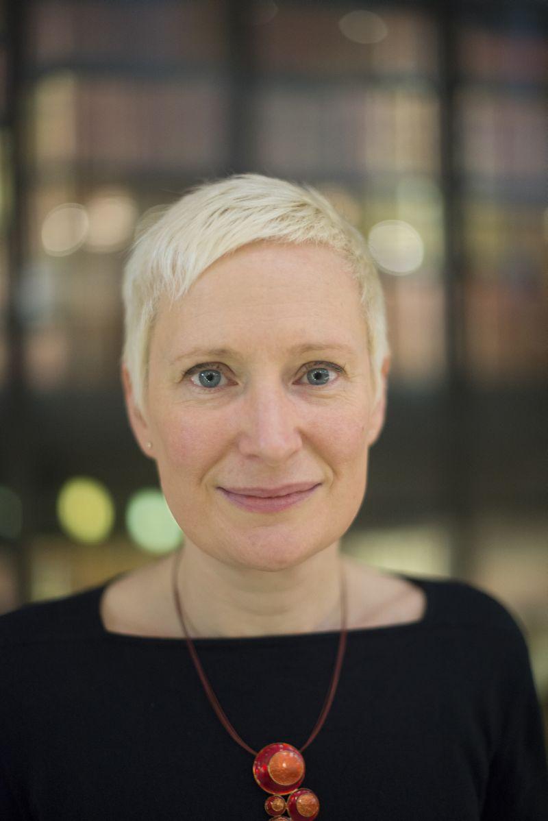 A woman with short cropped blonde hair smiles and looks directly at the camera.