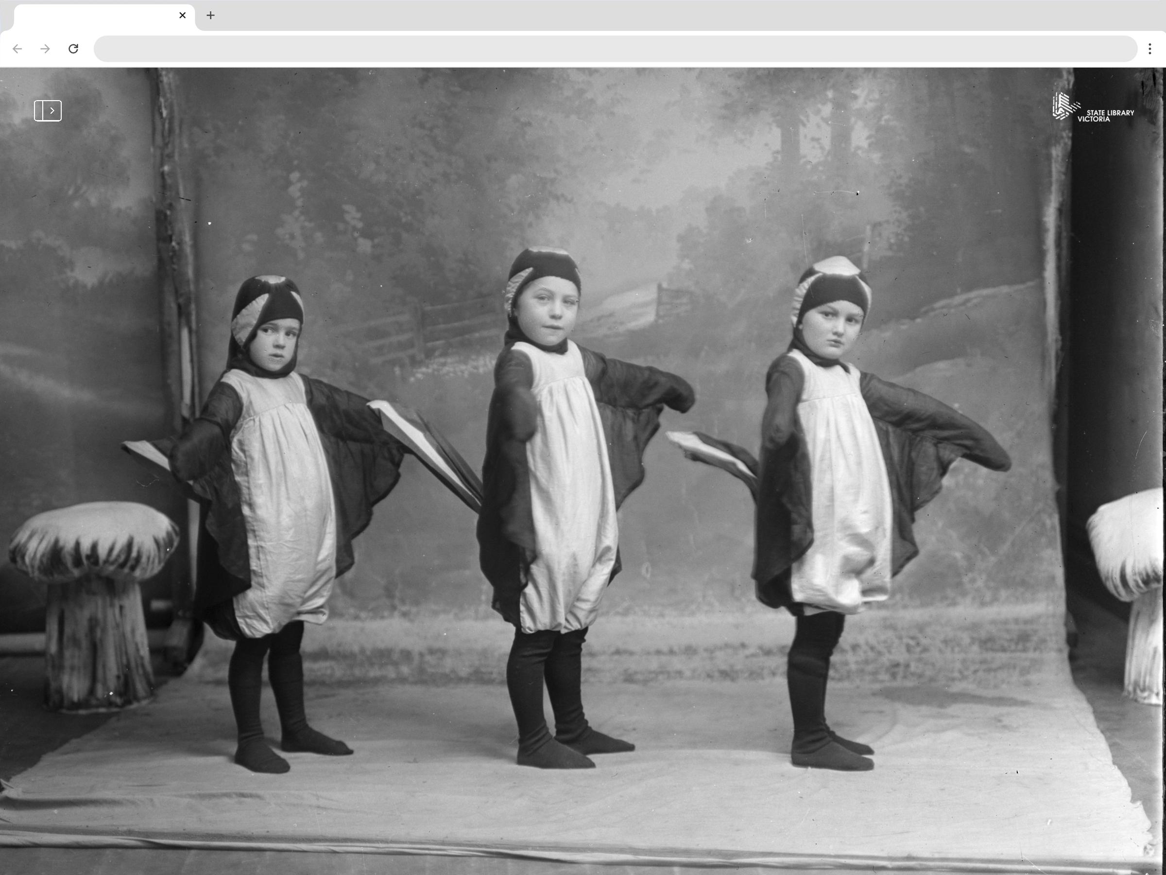 Three children in penguin costumes, lined up in a photographers studio. Black and white.