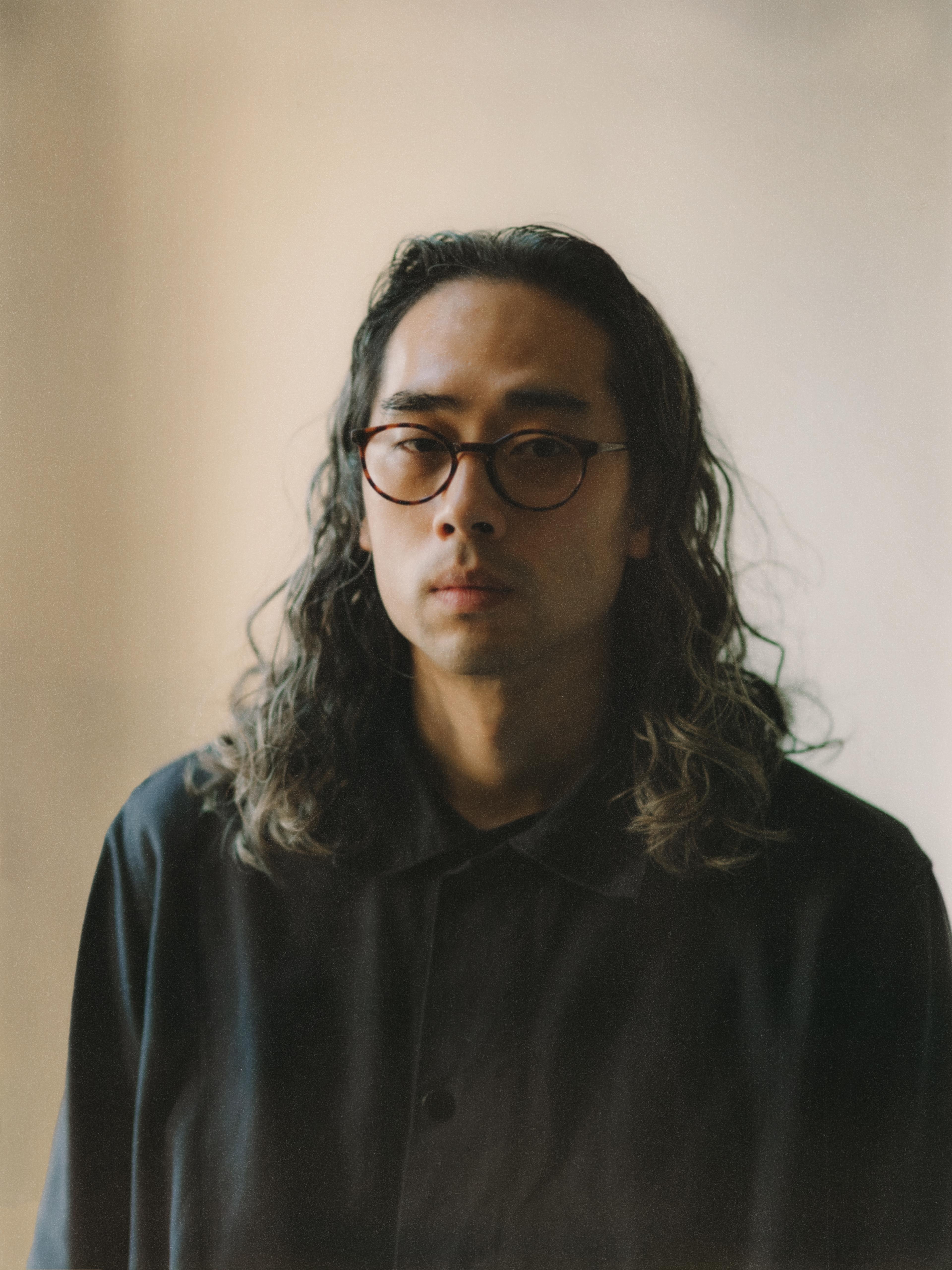 Man with glasses, and long hair, facing the camera. He wears a dark top.
