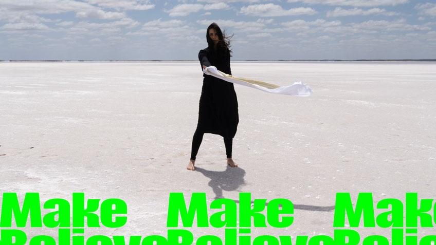 A woman with dark hair and dressed predominantly in black, standing n a vast deserted landscape. Bright green text overlays the image.