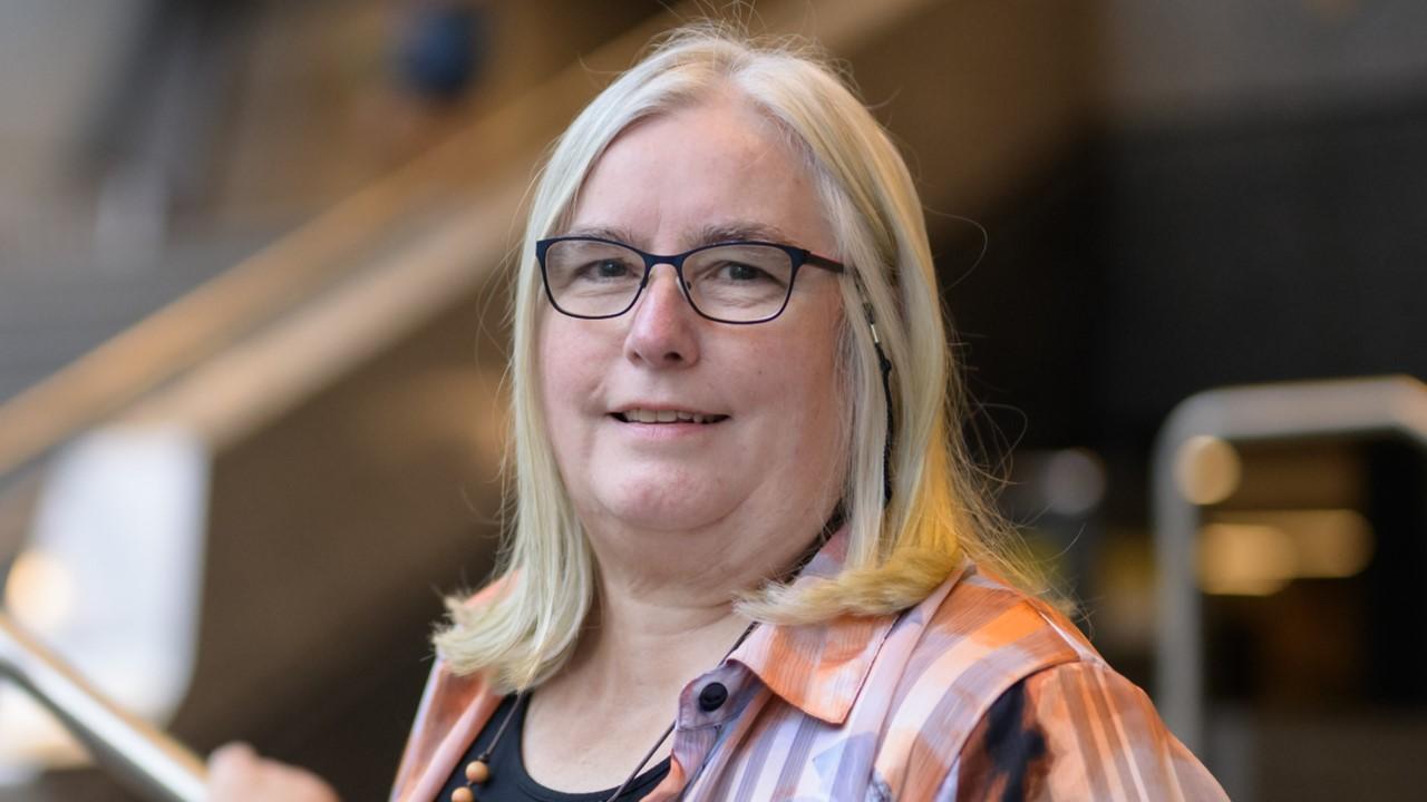 A closeup of a woman (Pru Mitchell) with black glasses and blonde hair 