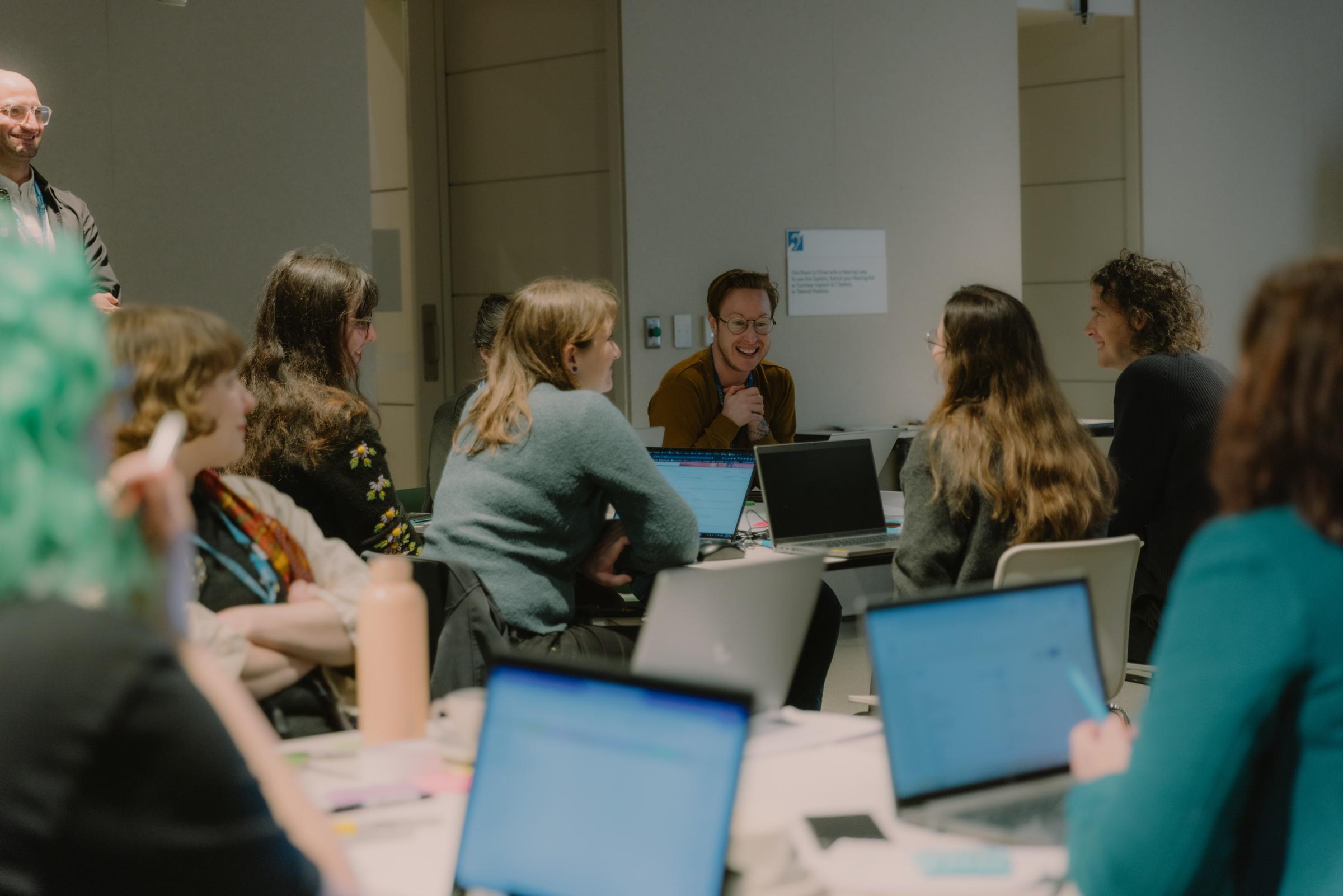 A smiling person - Phizz Telford - sitting at a workshop table with other participants