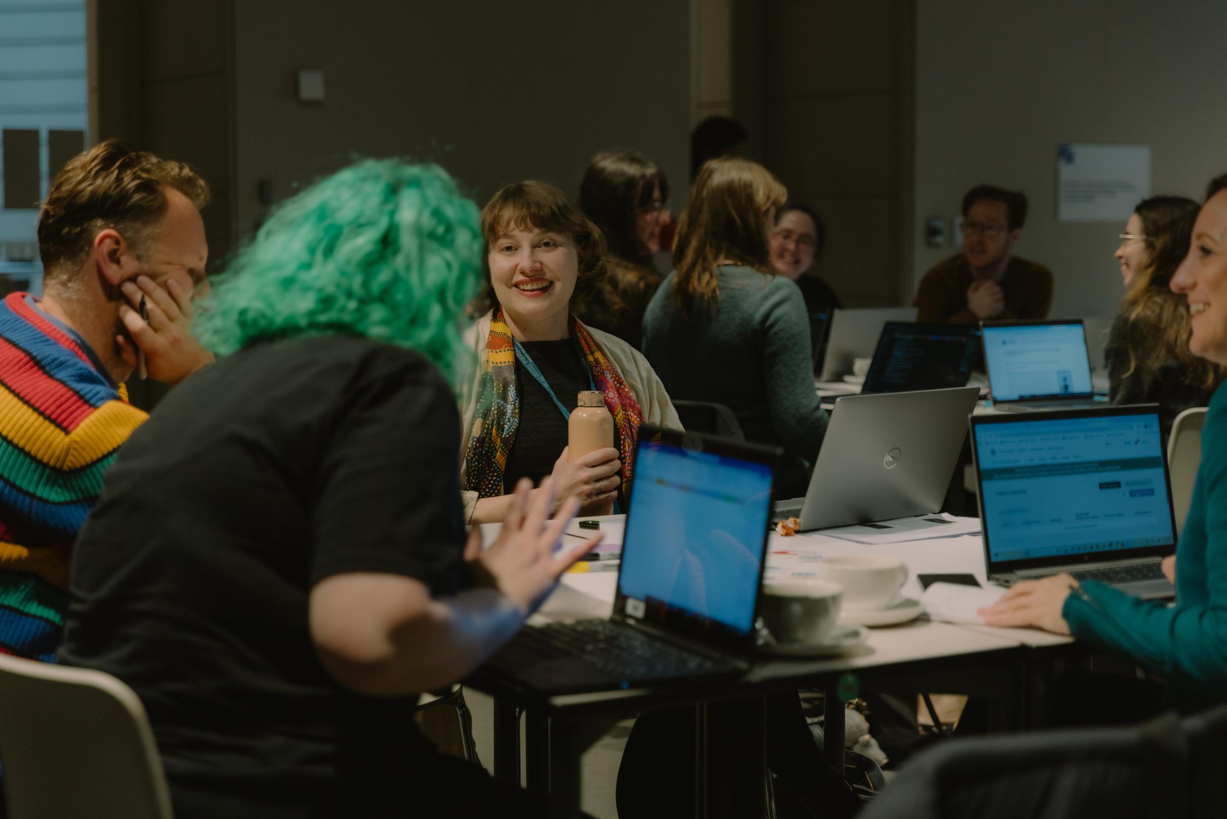 A young woman - Julia Rodwell - smiling at a green-haired person in a workshop surrounded by other participants