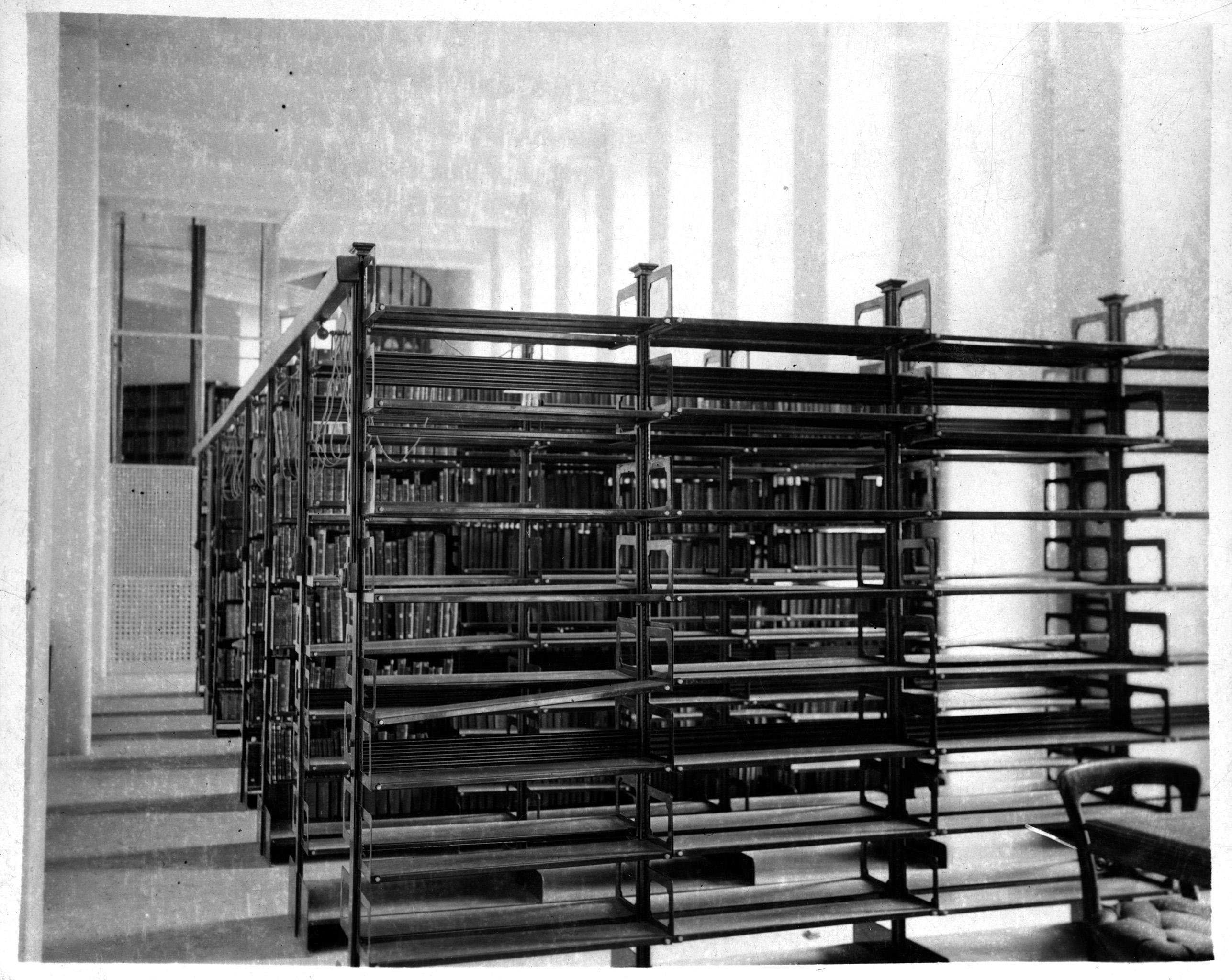 A black and white photograph of rows of empty steel shelves in a library hallway