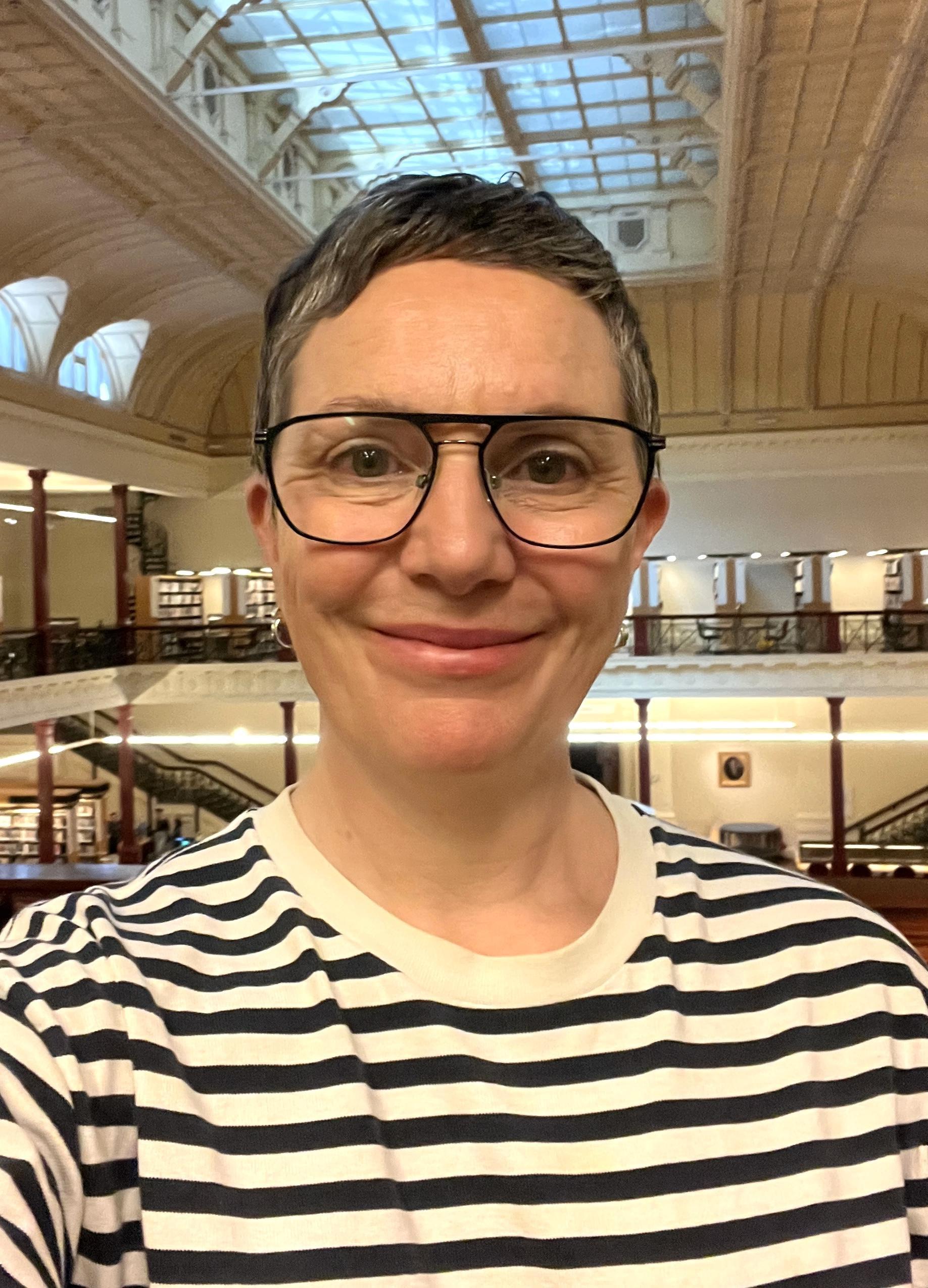 A closeup portrait image of a smiling woman (Ellen Spalding) with very short hair, black glasses and a striped top