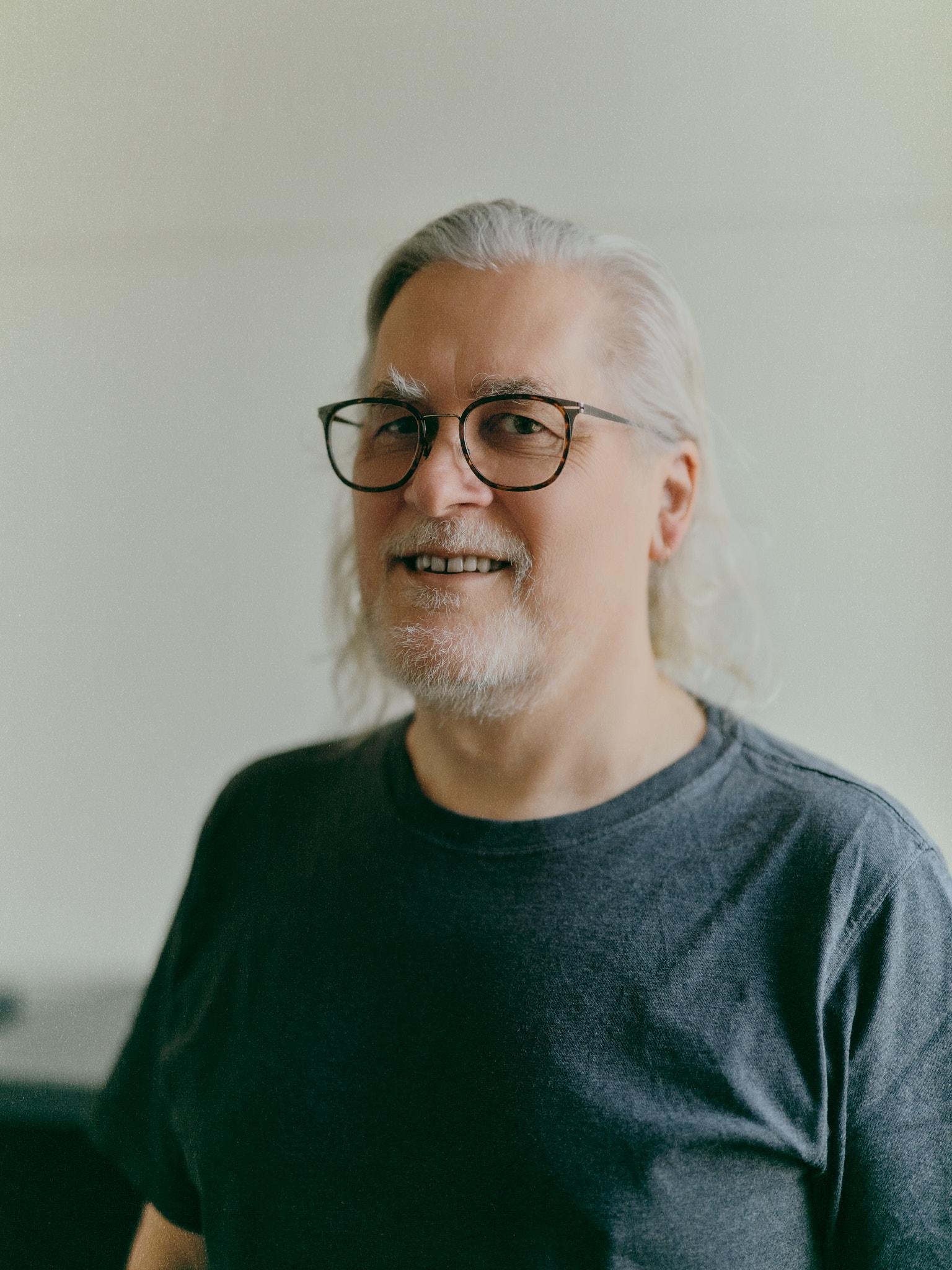 A portrait shot of a man (Tim Sherratt) with long grey hair wearing thick black glasses and a grey t-shirt