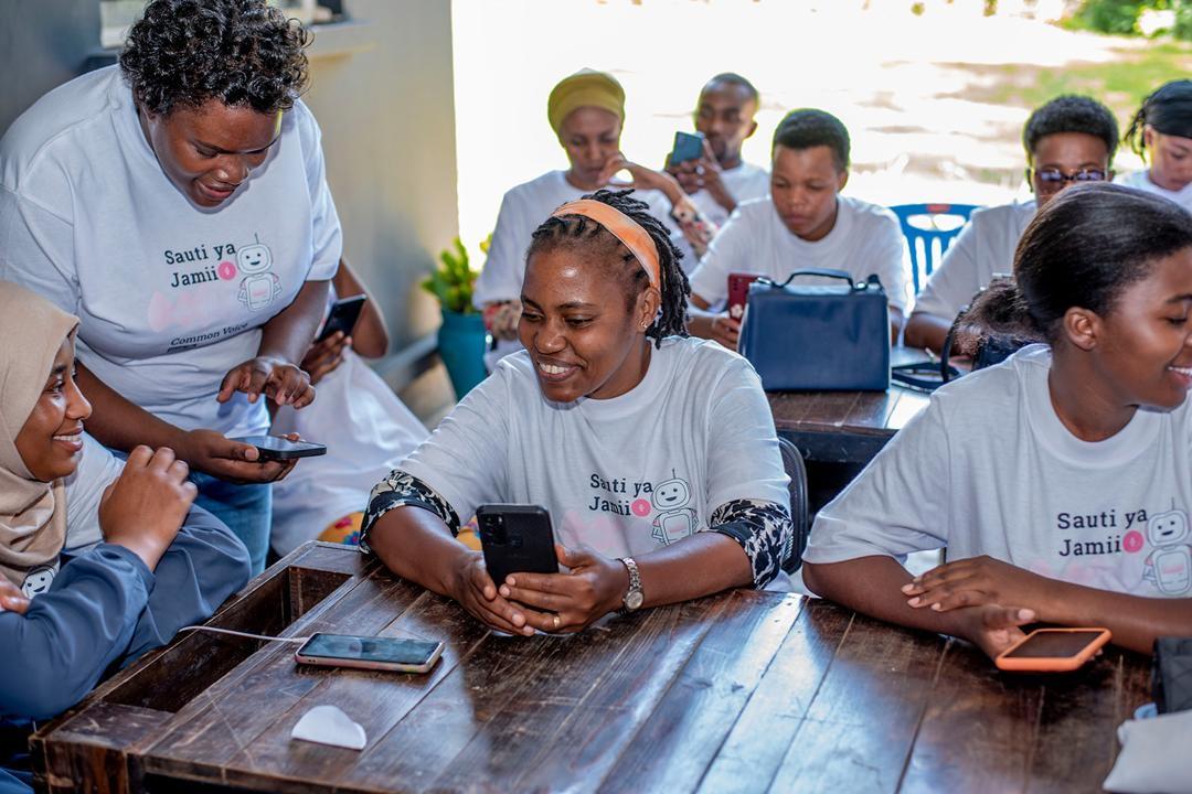 A group of smiling people of African origin sitting at a table looking at phones and conversing