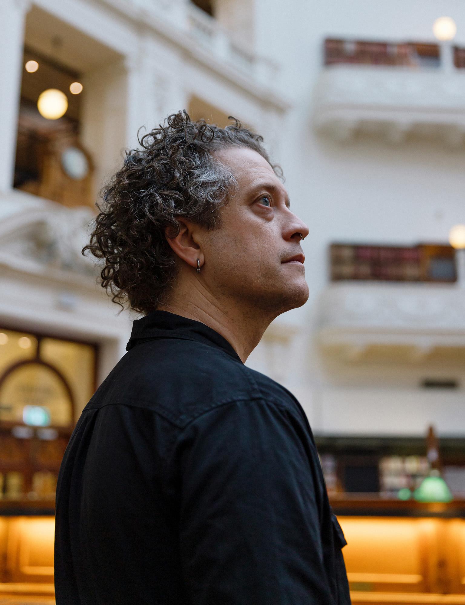 Side profile portrait of person with curly, greying hair wearing a black shirt