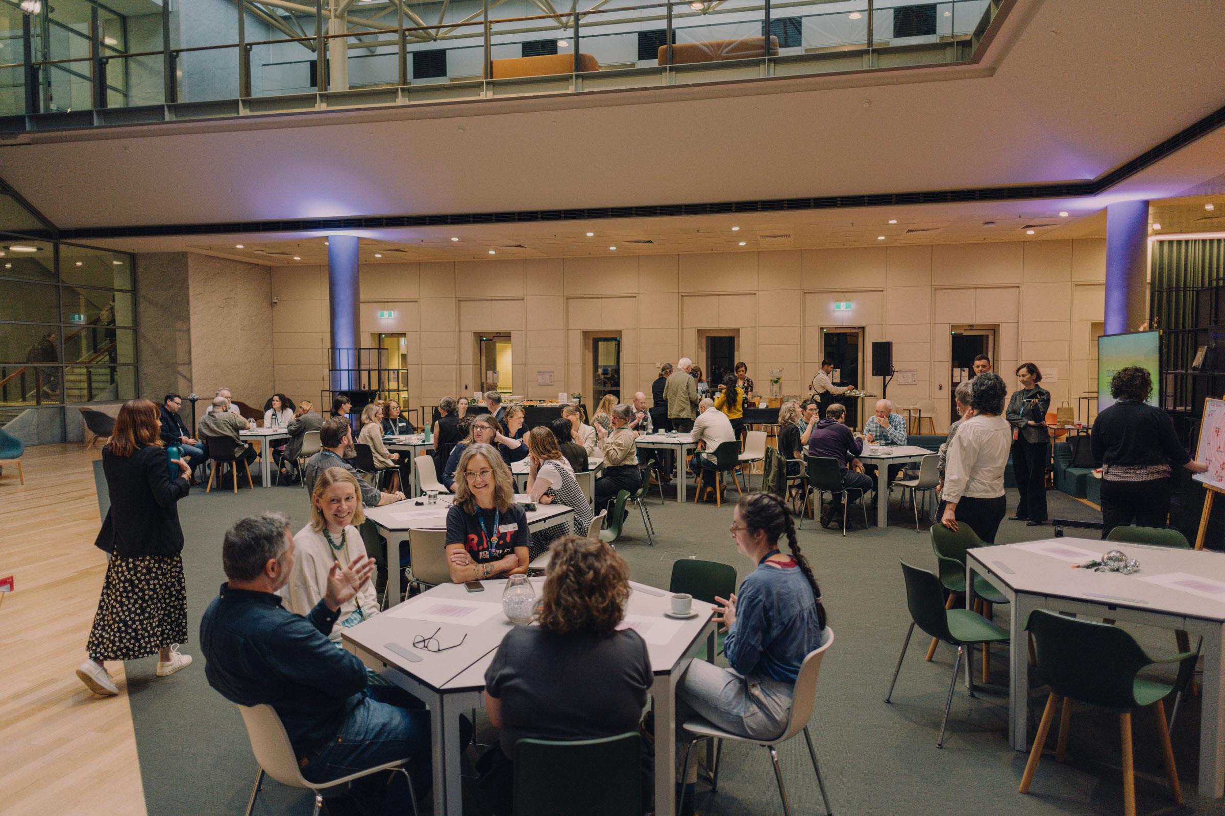 Groups of people sitting at hexagonal tables in a large conference space