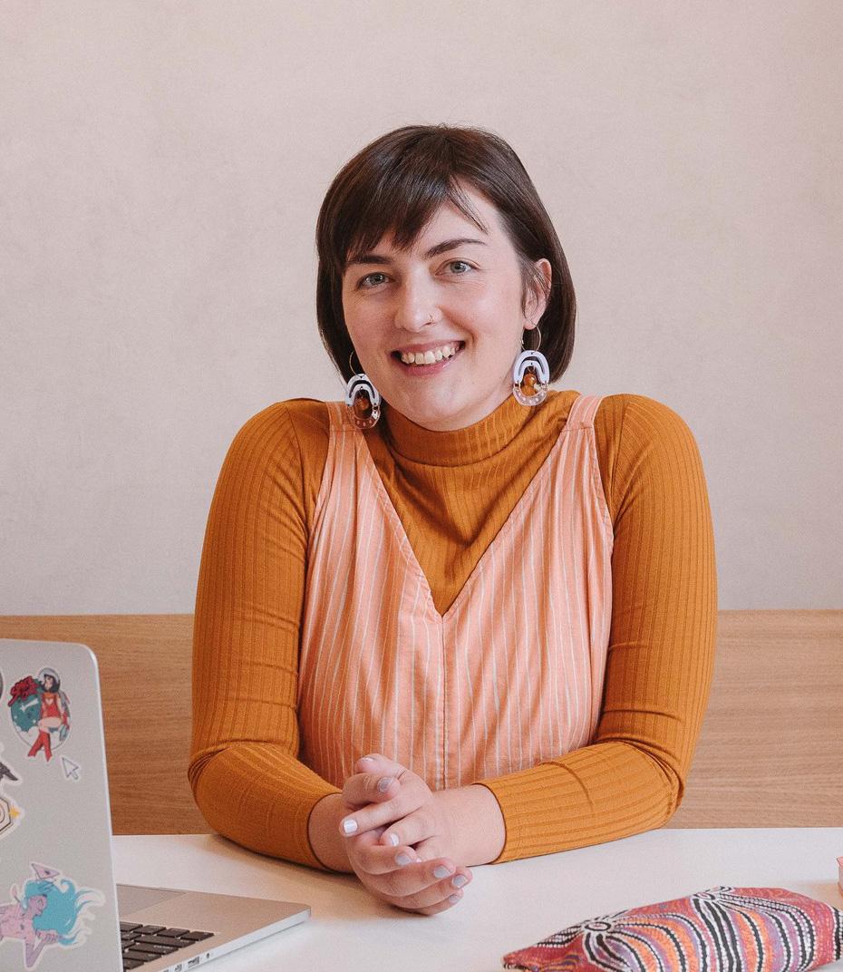 A woman with short brown hair wearing orange sitting at a table, smiling and facing the camera