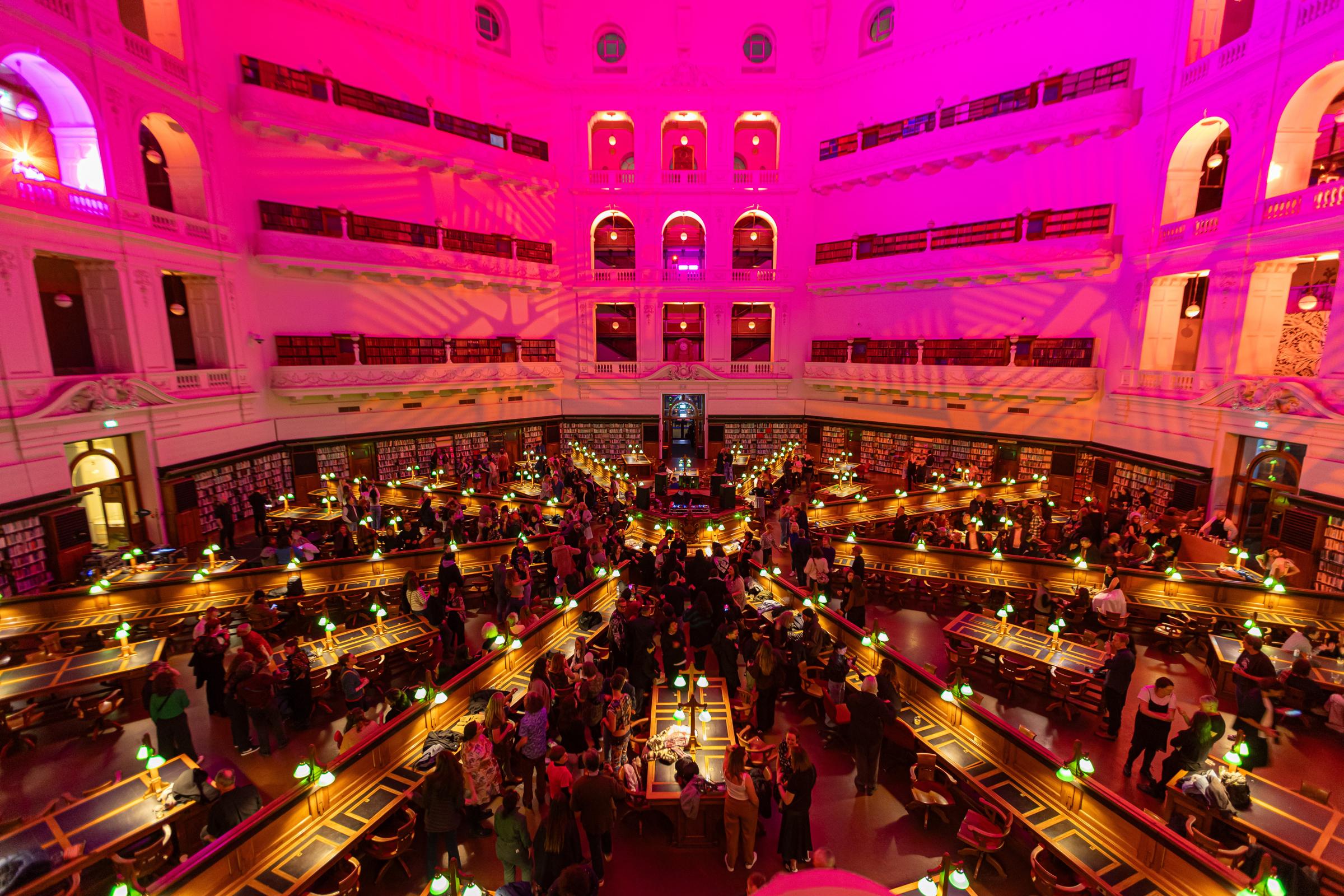 An aerial view of a grand hexagonal library space illuminated by warm pink and yellow lights