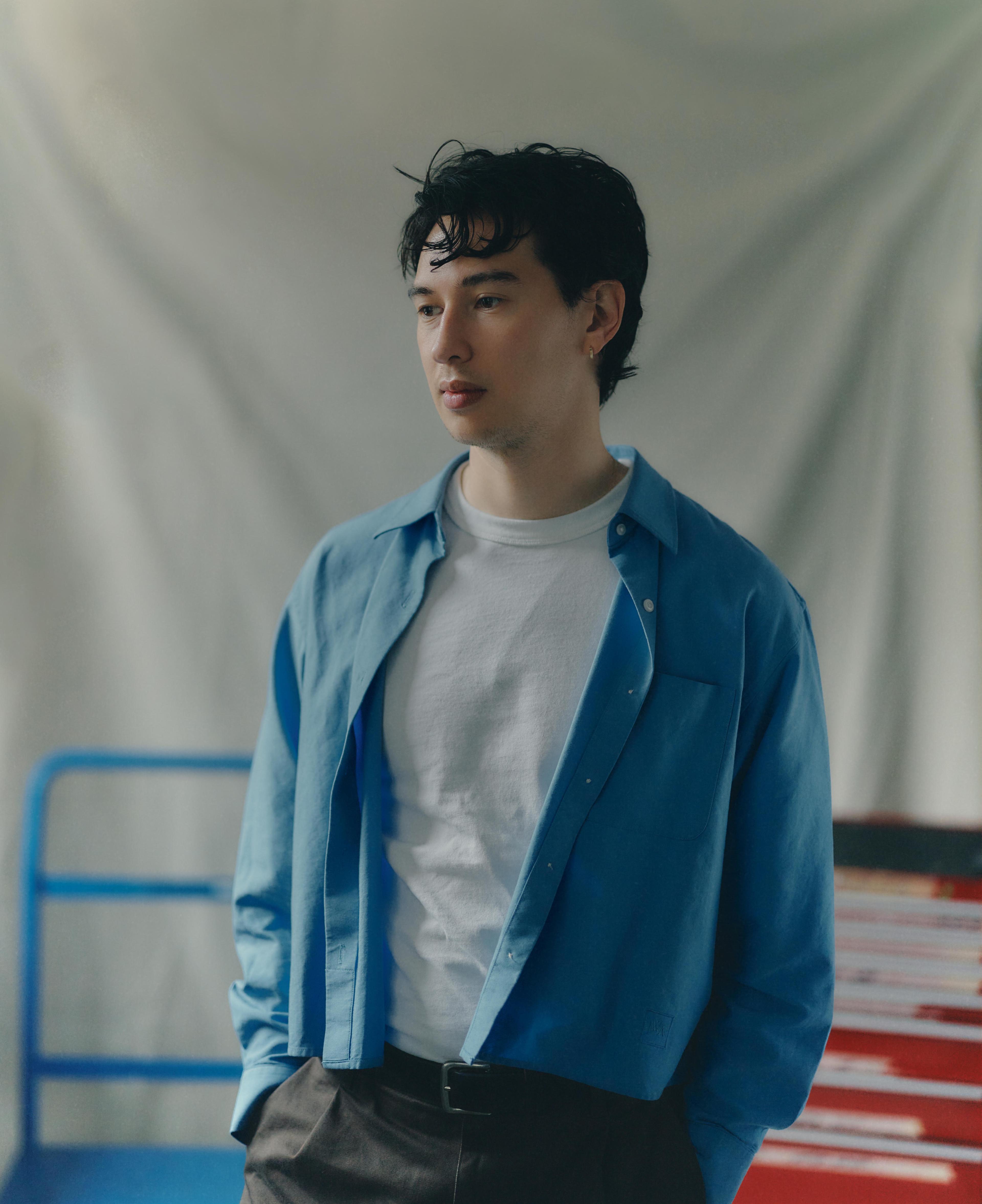 Portrait of a tall thin man (Lachlan Siu) with medium length black hair wearing a blue overshirt and white t-shirt looking to the left