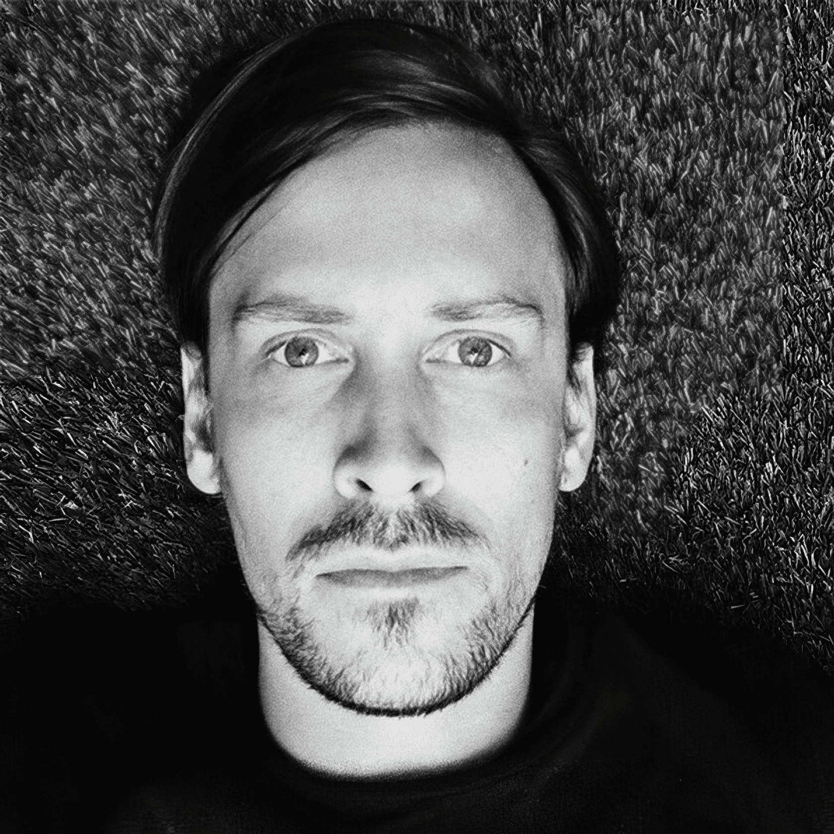 Headshot of a man with facial hair and dark side-swept hair, wearing a black shirt.