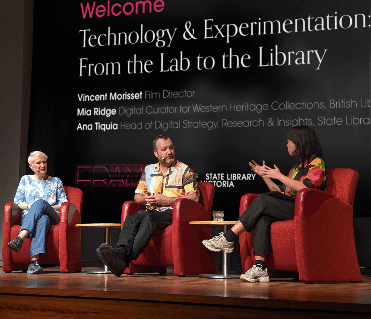Three people sitting and talking in red armchairs on stage in front of a screen reading 'Welcome. Technology & Experimentation: From the Lab to the Library".