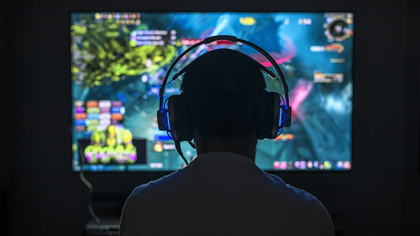A silhouetted head and shoulders, wearing large headphones in front of a colourful display screen.