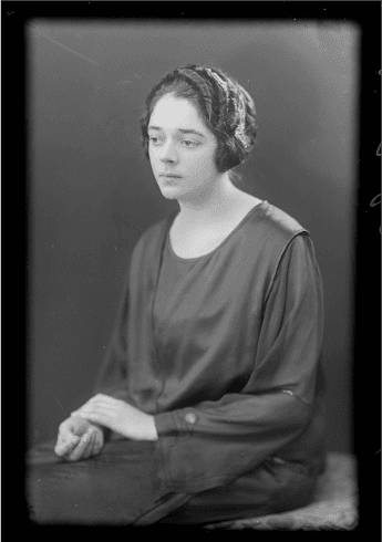 A black and white portrait of a woman, Mrs F. McDonald. She has a pensive look on her face and she is looking to the left of frame. Her hands are crossed in her lap.