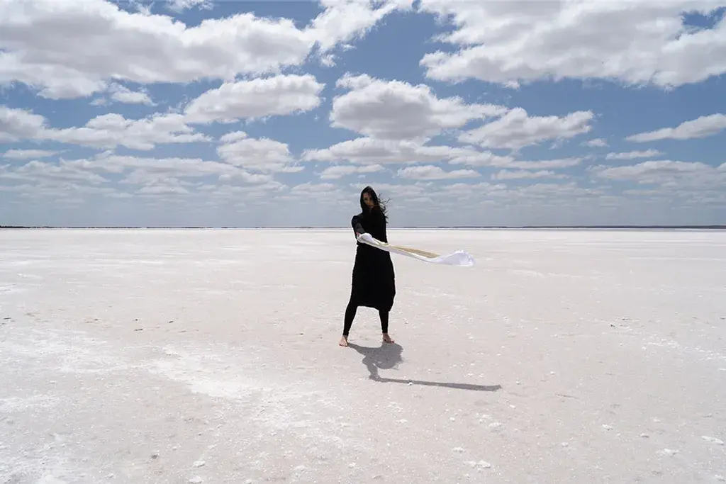 A woman in black in the desert holding a white scarf